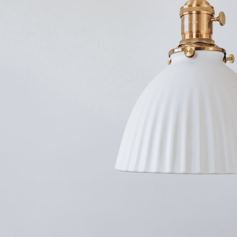 Pleated ceramic pendant light with brass gold fixture, close up detail.