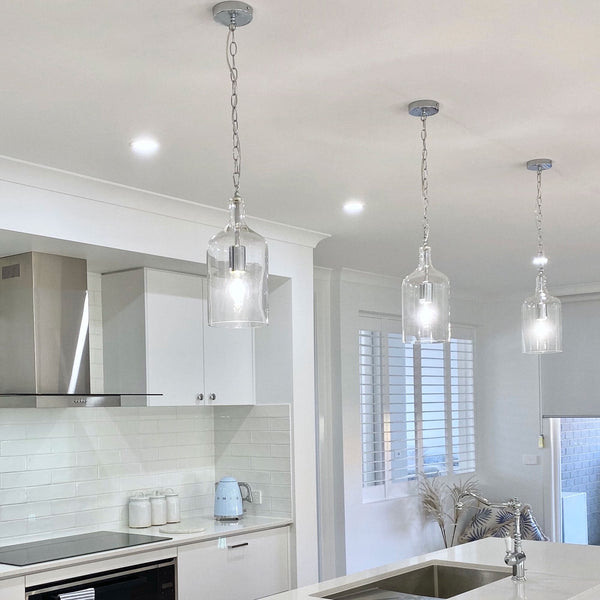 glass pendant light with chrome hardware and adjustable chain hanging in a white kitchen