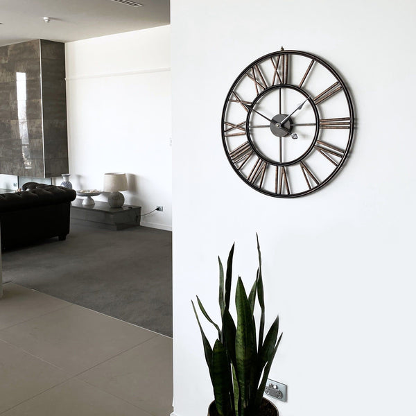 large black bronze metal wall clock on a white wall in a modern living room