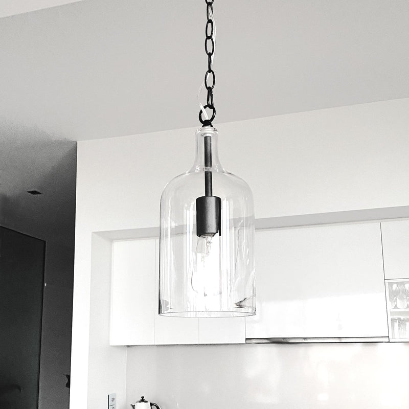 glass pendant light with black hardware and adjustable chain hanging  in a white kitchen