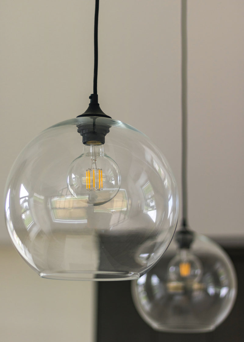 A modern glass pendant light with a clear round shade, suspended from a sleek cord, emitting warm white light.