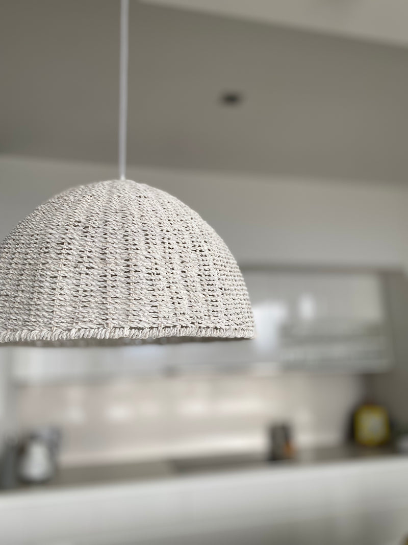 Whitewash rope pendant light suspended from the ceiling, emitting a soft, warm glow, perfect for rustic or coastal-themed interiors.