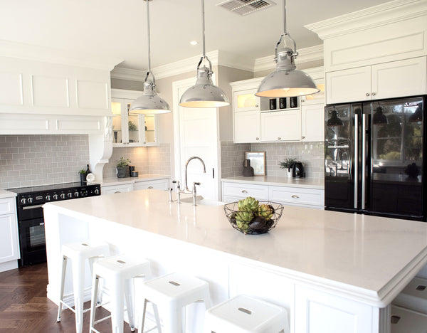 industrial chrome pendant lights in a bright white kitchen with black stove and fridge and white bar stools